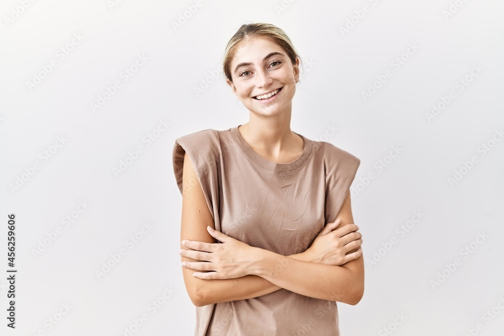 Young blonde woman standing over isolated background happy face smiling with crossed arms looking at the camera. positive person. Young blonde woman standing over isolated background happy face smiling with crossed arms looking at the camera. positive person.