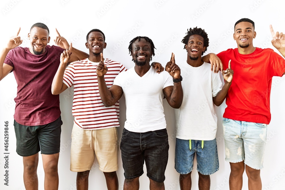 Obraz premium Young african group of friends standing together over isolated background smiling amazed and surprised and pointing up with fingers and raised arms.