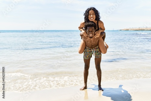 Young african american man holding girlfriend on his back at the beach. © Krakenimages.com