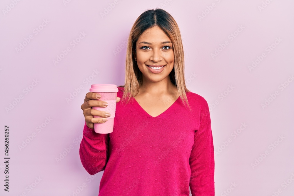 Beautiful hispanic woman drinking a take away cup of coffee looking positive and happy standing and smiling with a confident smile showing teeth Beautiful hispanic woman drinking a take away cup of coffee looking positive and happy standing and smiling with a confident smile showing teeth