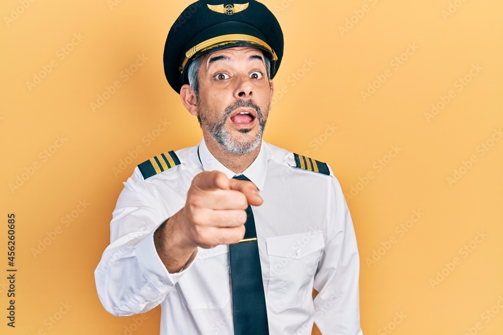 Handsome middle age man with grey hair wearing airplane pilot uniform pointing displeased and frustrated to the camera, angry and furious with you Handsome middle age man with grey hair wearing airplane pilot uniform pointing displeased and frustrated to the camera, angry and furious with you