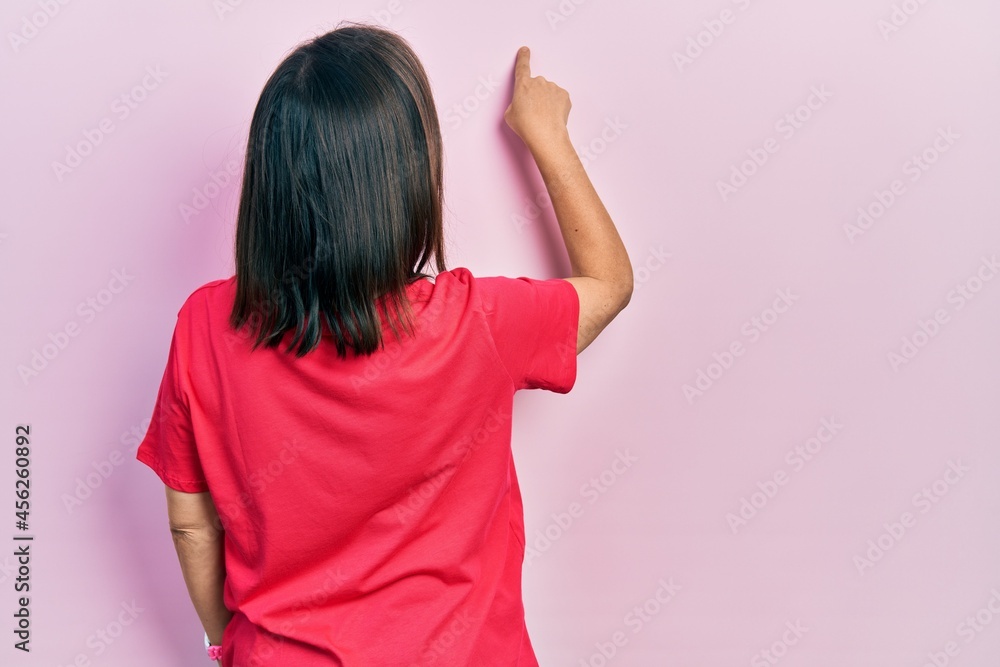 Middle age hispanic woman wearing casual clothes posing backwards pointing ahead with finger hand Middle age hispanic woman wearing casual clothes posing backwards pointing ahead with finger hand