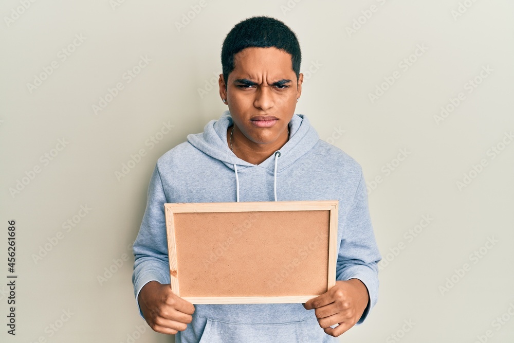 Young handsome hispanic man holding empty corkboard skeptic and nervous, frowning upset because of problem. negative person.