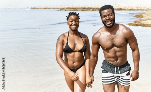 Young african american tourist couple wearing swimwear walking with hands together at the beach.