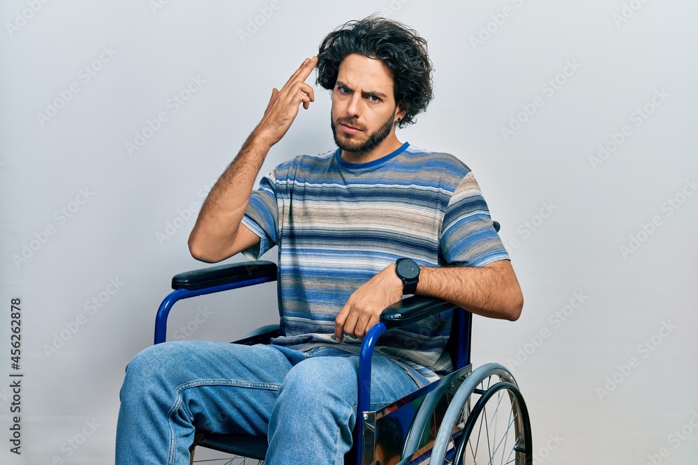 Handsome hispanic man sitting on wheelchair shooting and killing oneself pointing hand and fingers to head like gun, suicide gesture. Handsome hispanic man sitting on wheelchair shooting and killing oneself pointing hand and fingers to head like gun, suicide gesture.