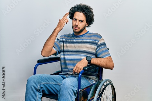 Handsome hispanic man sitting on wheelchair shooting and killing oneself pointing hand and fingers to head like gun, suicide gesture.