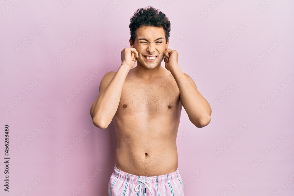 Fototapeta premium Young handsome man wearing swimwear shirtless covering ears with fingers with annoyed expression for the noise of loud music. deaf concept.