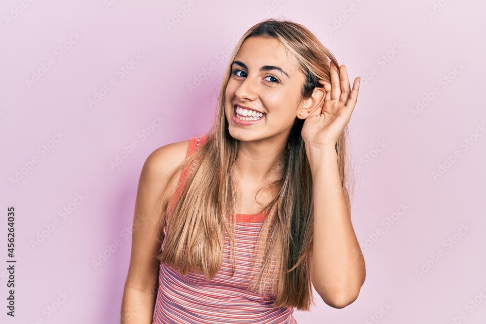 Beautiful hispanic woman wearing casual summer t shirt smiling with hand over ear listening an hearing to rumor or gossip. deafness concept. Beautiful hispanic woman wearing casual summer t shirt smiling with hand over ear listening an hearing to rumor or gossip. deafness concept.