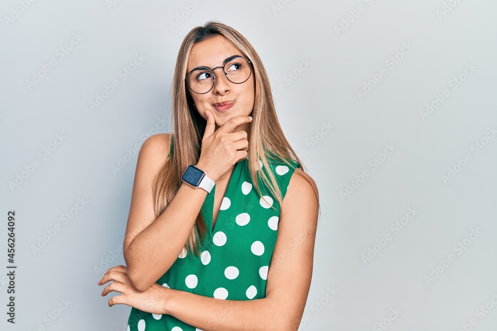 Beautiful hispanic woman wearing elegant shirt and glasses with hand on chin thinking about question, pensive expression. smiling with thoughtful face. doubt concept. Beautiful hispanic woman wearing elegant shirt and glasses with hand on chin thinking about question, pensive expression. smiling with thoughtful face. doubt concept.
