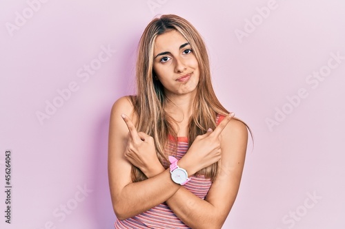 Beautiful hispanic woman wearing casual summer t shirt pointing to both sides with fingers, different direction disagree