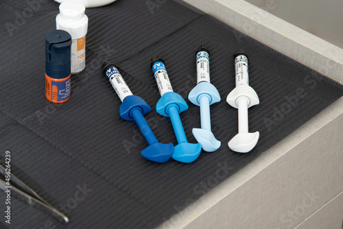 cuatro jeringas con composite dental, espejo, explorador y pinzas dentales en la mesa de trabajo de un odontólogo