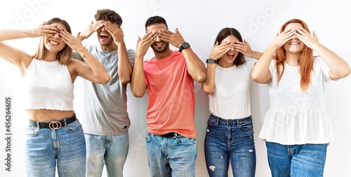 Group of young friends standing together over isolated background covering eyes with hands smiling cheerful and funny. blind concept.