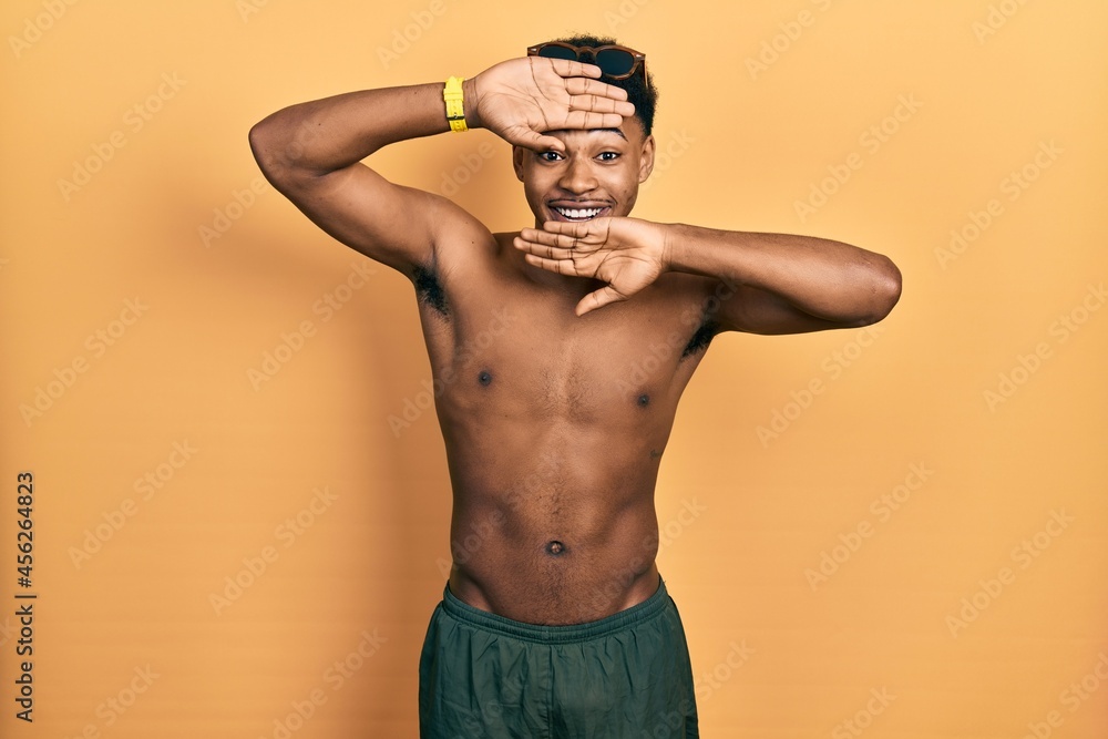 Fototapeta premium Young african american man wearing swimwear and swimmer glasses smiling cheerful playing peek a boo with hands showing face. surprised and exited