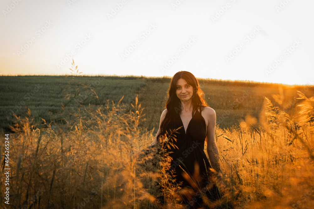 Sunset, soft golden evening colors, young, beautiful, emotional brunette girl with long hair in a black long dress on a golden wheat field. Cosiness of soul, joy, nature Sunset, soft golden evening colors, young, beautiful, emotional brunette girl with long hair in a black long dress on a golden wheat field. Cosiness of soul, joy, nature