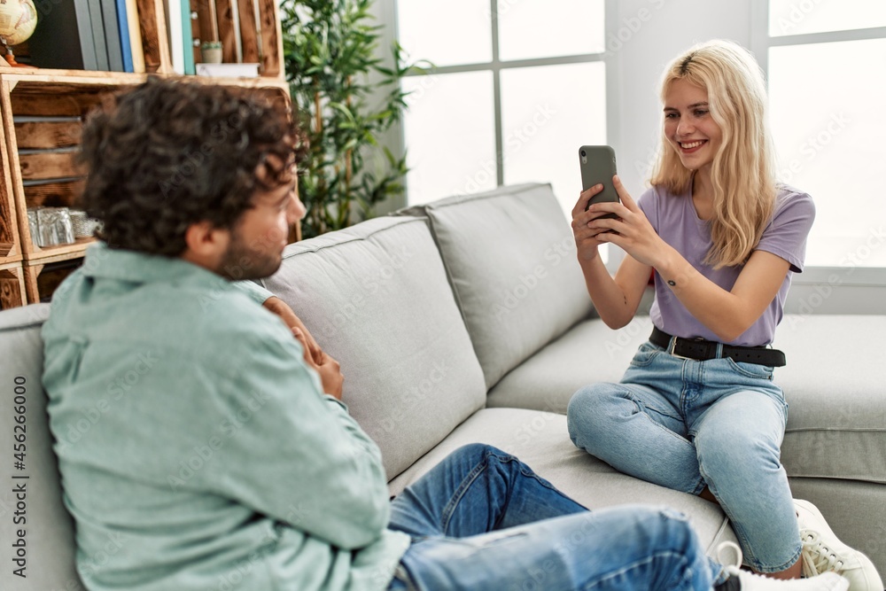 Fototapeta premium Young woman making picture of her boyfriend using smartphone at home