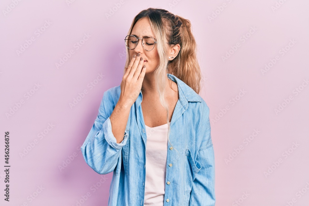 Beautiful young blonde woman wearing casual clothes and glasses bored yawning tired covering mouth with hand. restless and sleepiness. Beautiful young blonde woman wearing casual clothes and glasses bored yawning tired covering mouth with hand. restless and sleepiness.