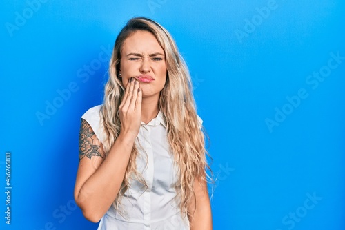 Beautiful young blonde woman wearing casual white shirt touching mouth with hand with painful expression because of toothache or dental illness on teeth. dentist