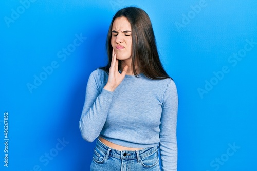 Young brunette teenager wearing casual sweater touching mouth with hand with painful expression because of toothache or dental illness on teeth. dentist © Krakenimages.com