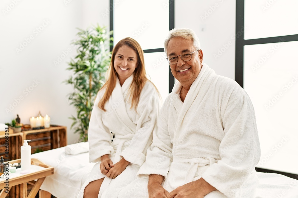 Middle age hispanic couple wearing bathrobe at wellness spa looking positive and happy standing and smiling with a confident smile showing teeth Middle age hispanic couple wearing bathrobe at wellness spa looking positive and happy standing and smiling with a confident smile showing teeth