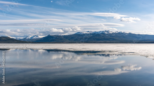 Stunning landscape view of mountains, with reflection in calm lake water below and stunning, bright blue sky. 