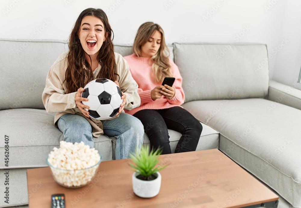 Girl smiling happy watching soccer match and her girlfriend boring using smartphone at home. Girl smiling happy watching soccer match and her girlfriend boring using smartphone at home.