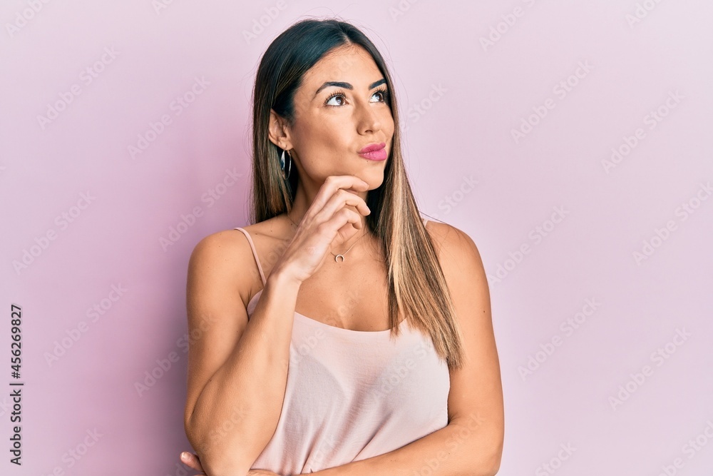 Young hispanic woman wearing casual sleeveless t shirt thinking concentrated about doubt with finger on chin and looking up wondering Young hispanic woman wearing casual sleeveless t shirt thinking concentrated about doubt with finger on chin and looking up wondering