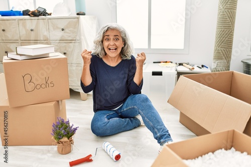 Middle age woman with grey hair sitting on the floor at new home screaming proud, celebrating victory and success very excited with raised arms photo