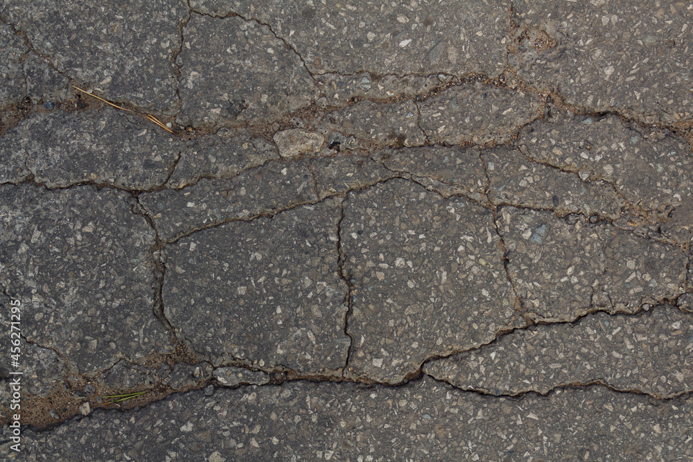 Obraz premium The texture of an asphalt road passing through the village. The road to the village. Dark-grey background texture of asphalt. Cracks in the asphalt. Destruction of the road