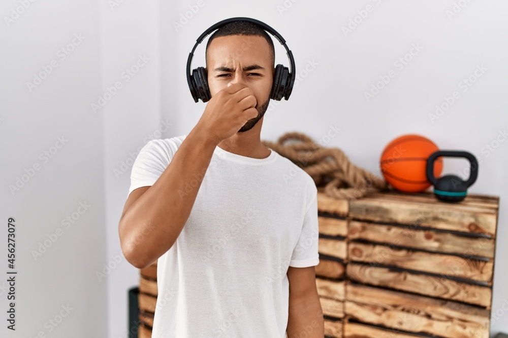 African american man listening to music using headphones at the gym smelling something stinky