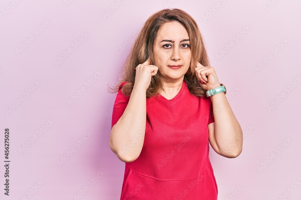 Middle age caucasian woman wearing casual clothes covering ears with fingers with annoyed expression for the noise of loud music. deaf concept. Middle age caucasian woman wearing casual clothes covering ears with fingers with annoyed expression for the noise of loud music. deaf concept.
