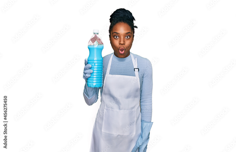 Young african american woman wearing apron holding detergent bottle scared and amazed with open mouth for surprise, disbelief face Young african american woman wearing apron holding detergent bottle scared and amazed with open mouth for surprise, disbelief face