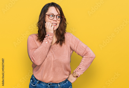 Fototapeta Young plus size woman wearing casual clothes and glasses looking stressed and nervous with hands on mouth biting nails
