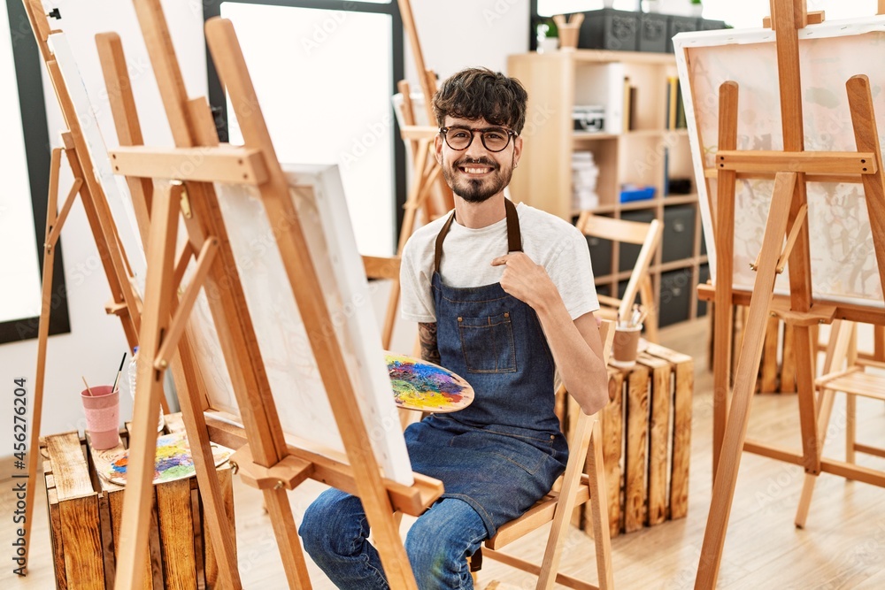 Hispanic man with beard at art studio pointing finger to one self smiling happy and proud