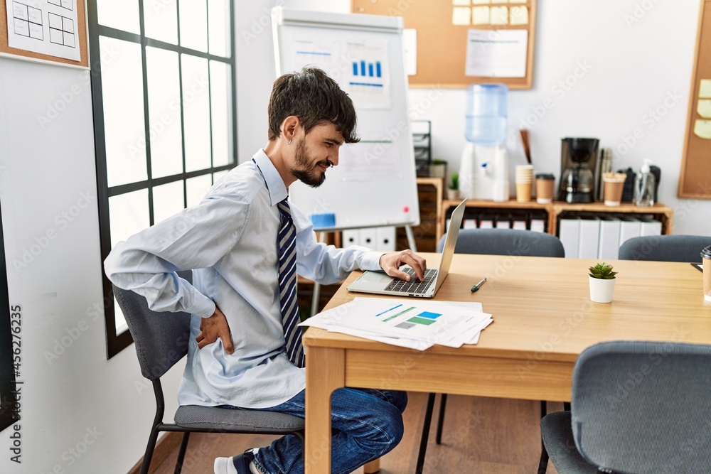 Young hispanic businessman with backache working at the office. Young hispanic businessman with backache working at the office.