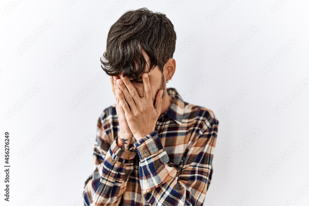 Hispanic man with beard standing over isolated background with sad expression covering face with hands while crying. depression concept. Hispanic man with beard standing over isolated background with sad expression covering face with hands while crying. depression concept.