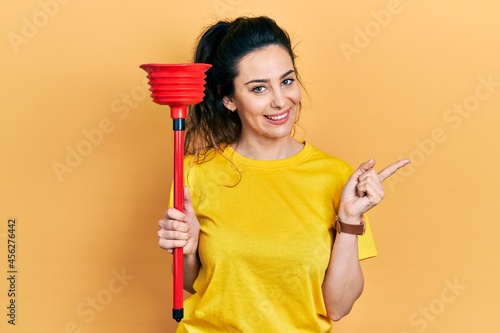Φωτογραφία Young hispanic woman holding toilet plunger smiling happy pointing with hand and