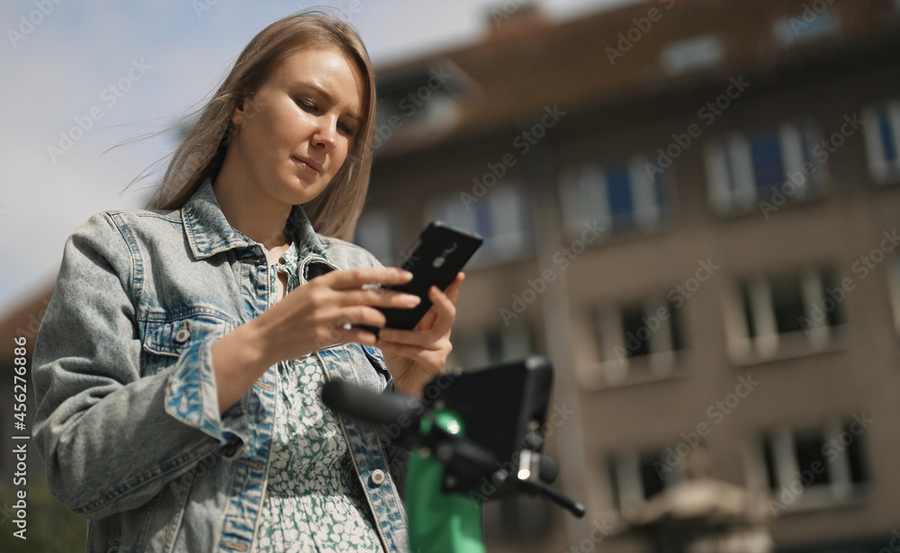 Woman using app on smartphone to unlock electric scooter on the street.