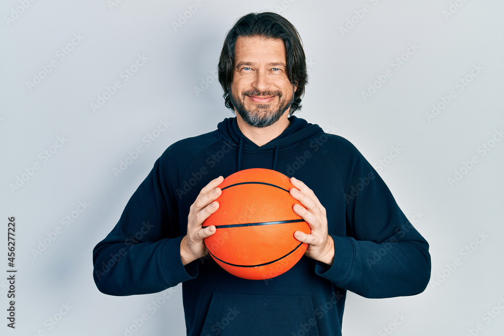 Middle age caucasian man holding basketball ball relaxed with serious expression on face. simple and natural looking at the camera.