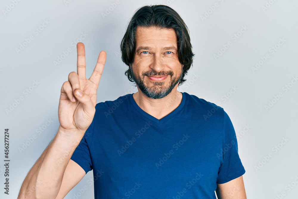 Fototapeta premium Middle age caucasian man wearing casual clothes smiling with happy face winking at the camera doing victory sign. number two.