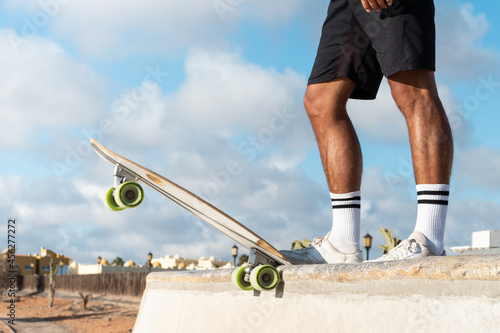 Skater legs at the top of the half pipe. Unrecognizable young skater at the skate park wearing summer clothes