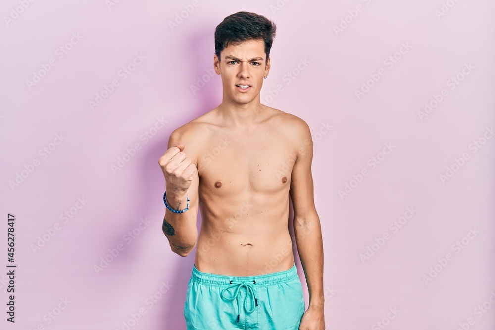 Fototapeta premium Young hispanic man wearing swimwear shirtless angry and mad raising fist frustrated and furious while shouting with anger. rage and aggressive concept.