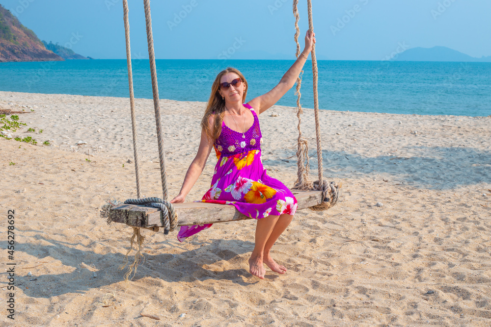 Young woman swinging on a swing suspended from a palm tree on the seashore. Travel and tourism to the tropical countries of Asia.