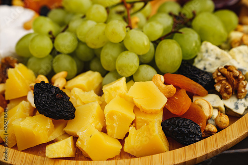 cheeses with grapes, dried fruits, nuts, honey and jam on a wooden plate.