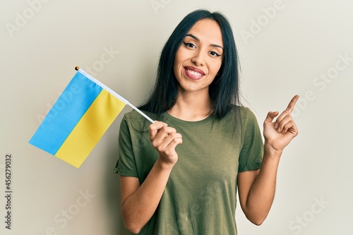 Young hispanic girl wearing ukraine flag smiling happy pointing with hand and finger to the side