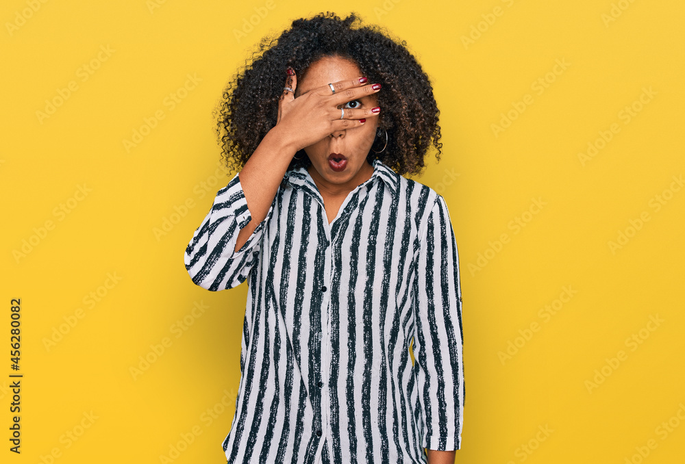 Young african american girl wearing casual clothes peeking in shock covering face and eyes with hand, looking through fingers with embarrassed expression. Young african american girl wearing casual clothes peeking in shock covering face and eyes with hand, looking through fingers with embarrassed expression.