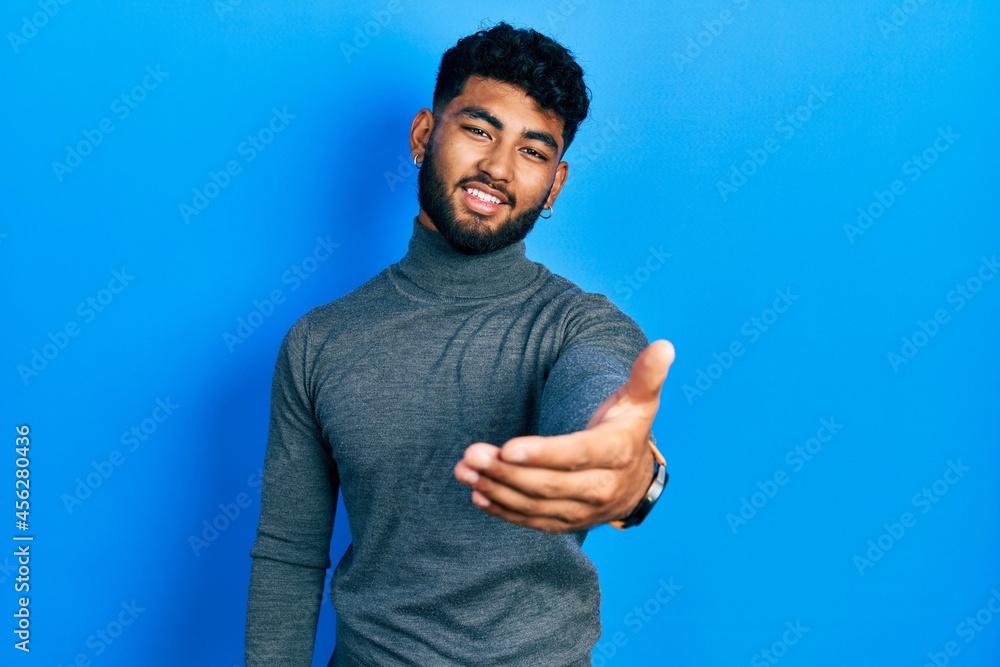 Arab man with beard wearing turtleneck sweater smiling cheerful offering palm hand giving assistance and acceptance. Arab man with beard wearing turtleneck sweater smiling cheerful offering palm hand giving assistance and acceptance.