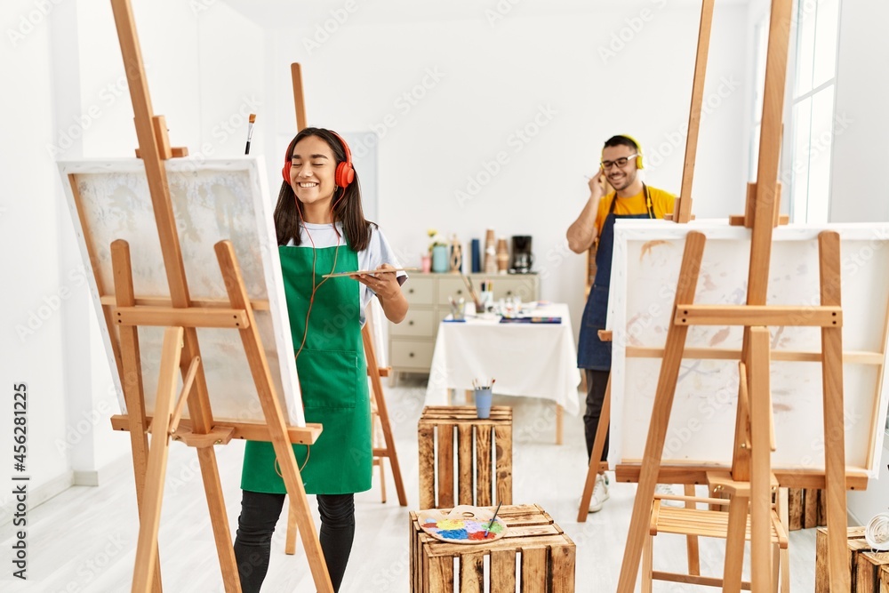 Young hispanic couple smiling happy listening to music and drawing at art studio.