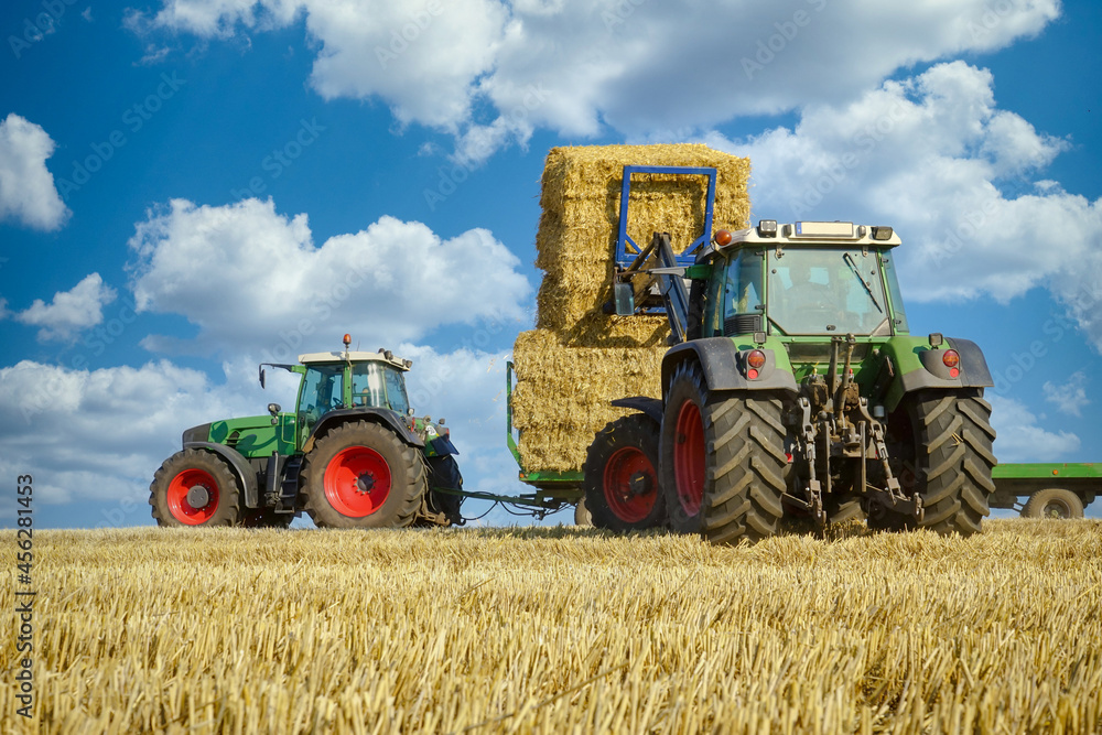 Strohernte - Traktor mit Frontlader beim Beladen eines Transportanhängers mit Strohballen. Strohernte - Traktor mit Frontlader beim Beladen eines Transportanhängers mit Strohballen.