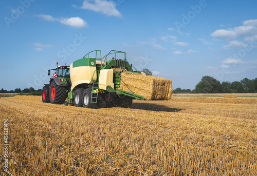 Strohernte - Traktor mit moderner Hochdruckpresse beim Pressen von Strohballen in Quaderform.