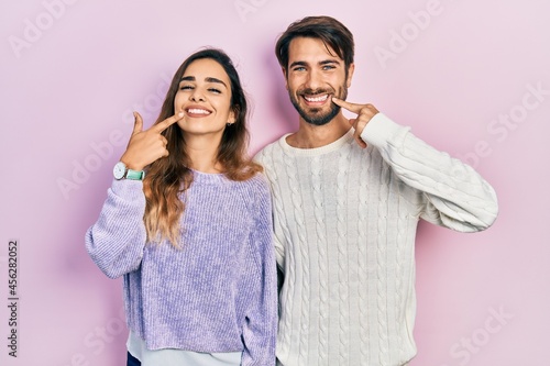 Young hispanic couple wearing casual clothes smiling cheerful showing and pointing with fingers teeth and mouth. dental health concept.